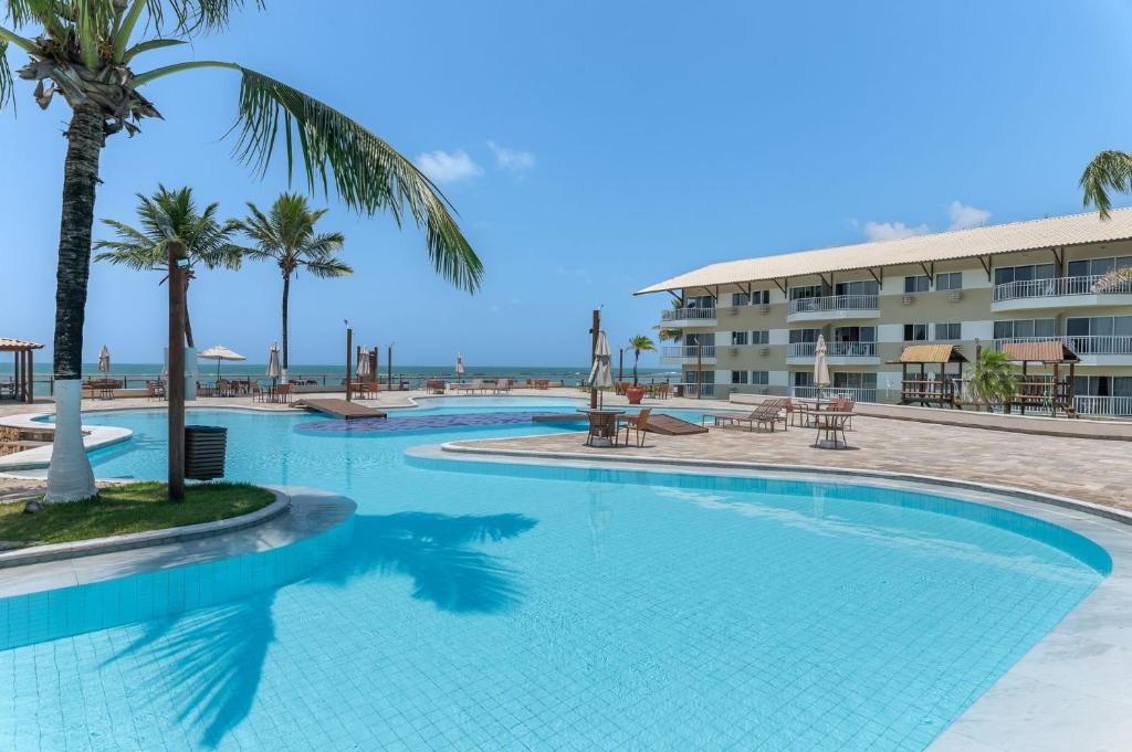 a large swimming pool with palm trees and a building at Flat Marupiara 220 - Muro Alto, Porto de Galinhas in Porto De Galinhas