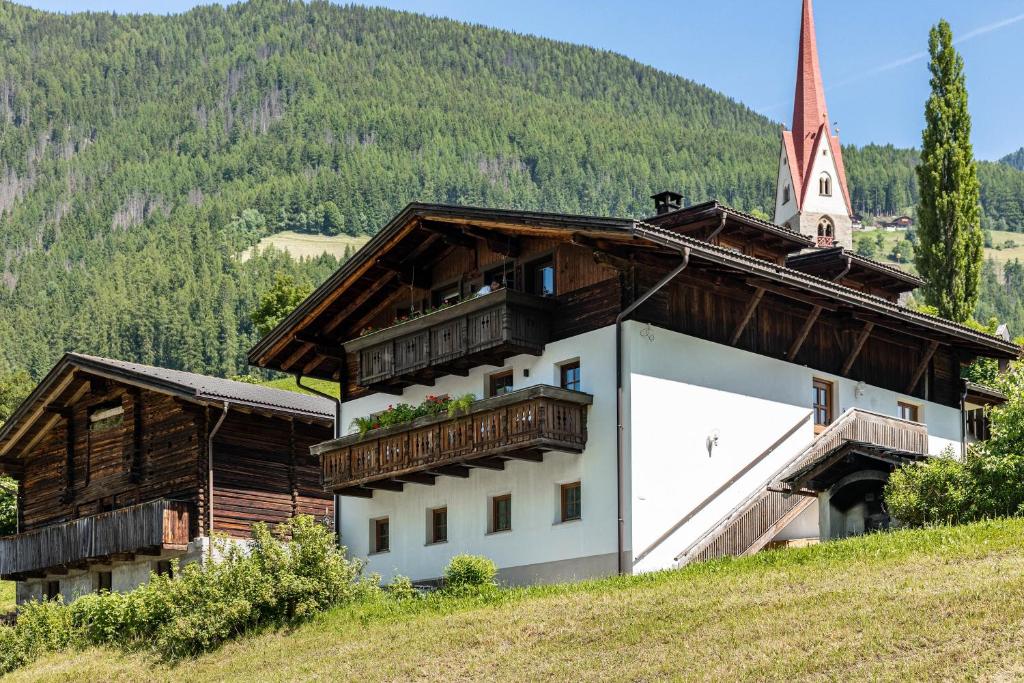 a building on a hill with a church in the background at Unterlacherhof Ahrntal in San Giacomo