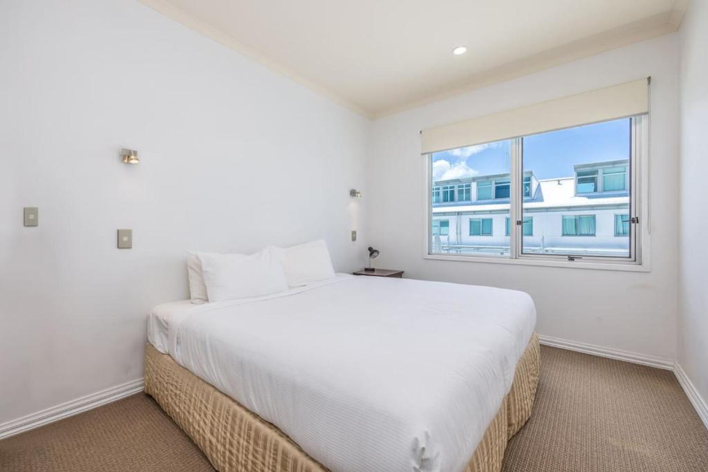 a white bedroom with a large bed and a window at QV Stays Waterfront Elegance on Princes Wharf in Auckland
