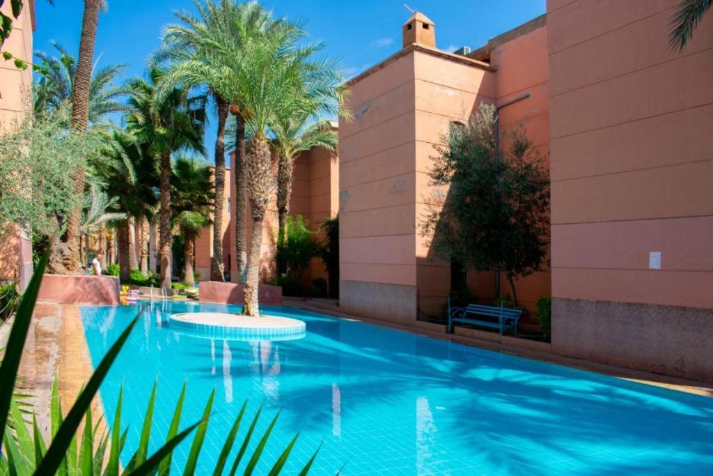 ein Swimmingpool mit Palmen vor einem Gebäude in der Unterkunft Riad Tamounte piscine palmeraie in Marrakesch