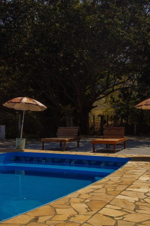 a swimming pool with two benches and an umbrella at Chácara da Moenda em Joanópolis in Joanópolis