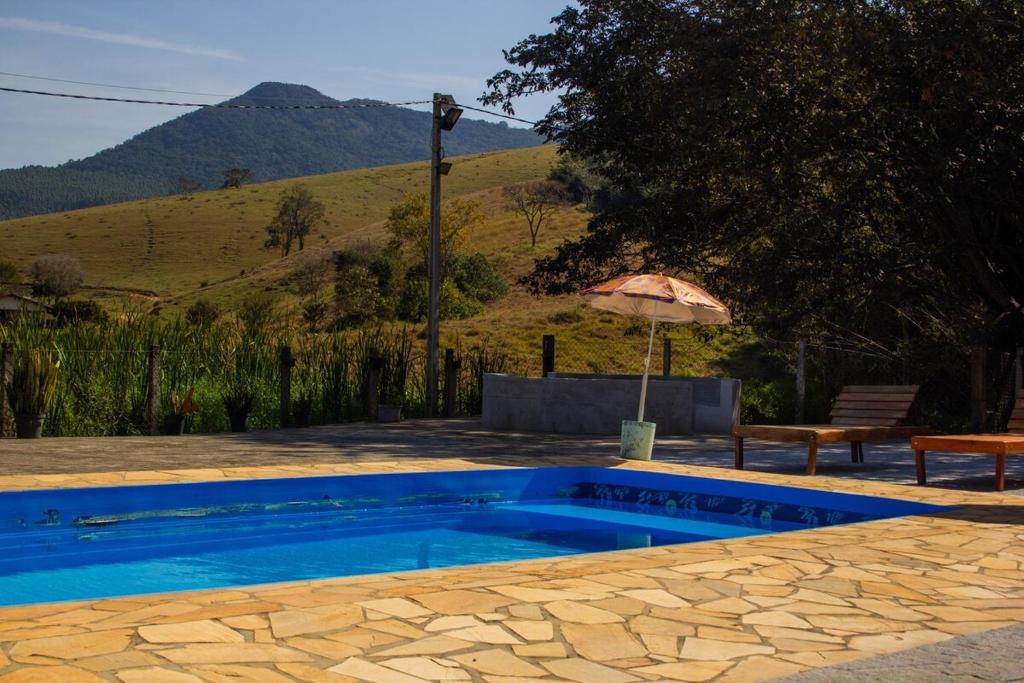 una piscina con ombrellone, tavolo e panca di Chácara da Moenda em Joanópolis a Joanópolis