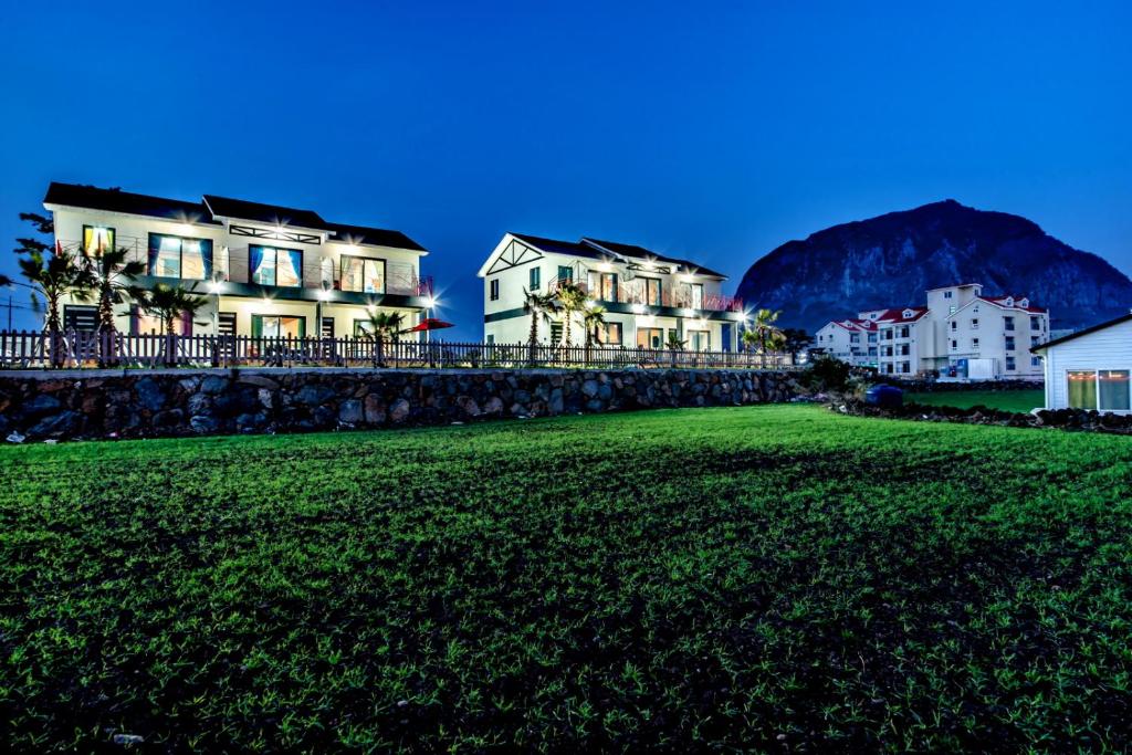 a row of houses on a beach with mountains in the background at Lohas Pension in Seogwipo