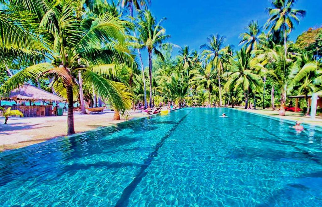 a large swimming pool next to a beach with palm trees at Blue Haven Bay Villas and Resort Apartments in Ko Chang