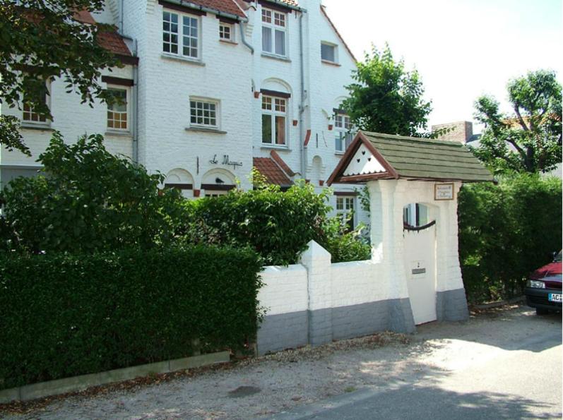 a white house with a gate and a garage at B&B Le Maquis in De Haan