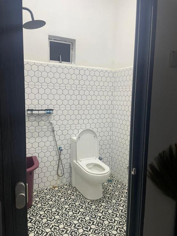 a bathroom with a toilet in a white tiled room at Villa Cempaka Homestay in Changlun