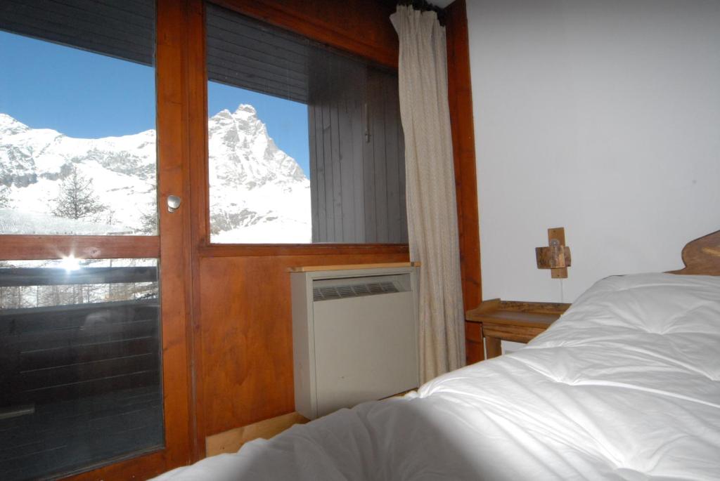 een slaapkamer met een bed en een raam met een met sneeuw bedekte berg bij Cromotherapy Apartment in Breuil-Cervinia