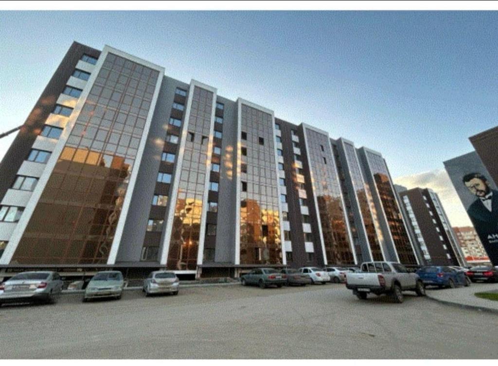 a large building with cars parked in a parking lot at Уральская 45А in Kostanay