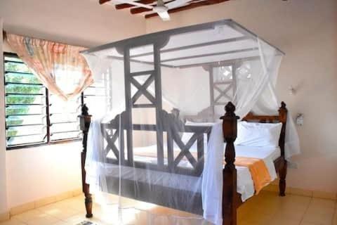 a bedroom with a canopy bed and a window at Kasuku villa in Ukunda