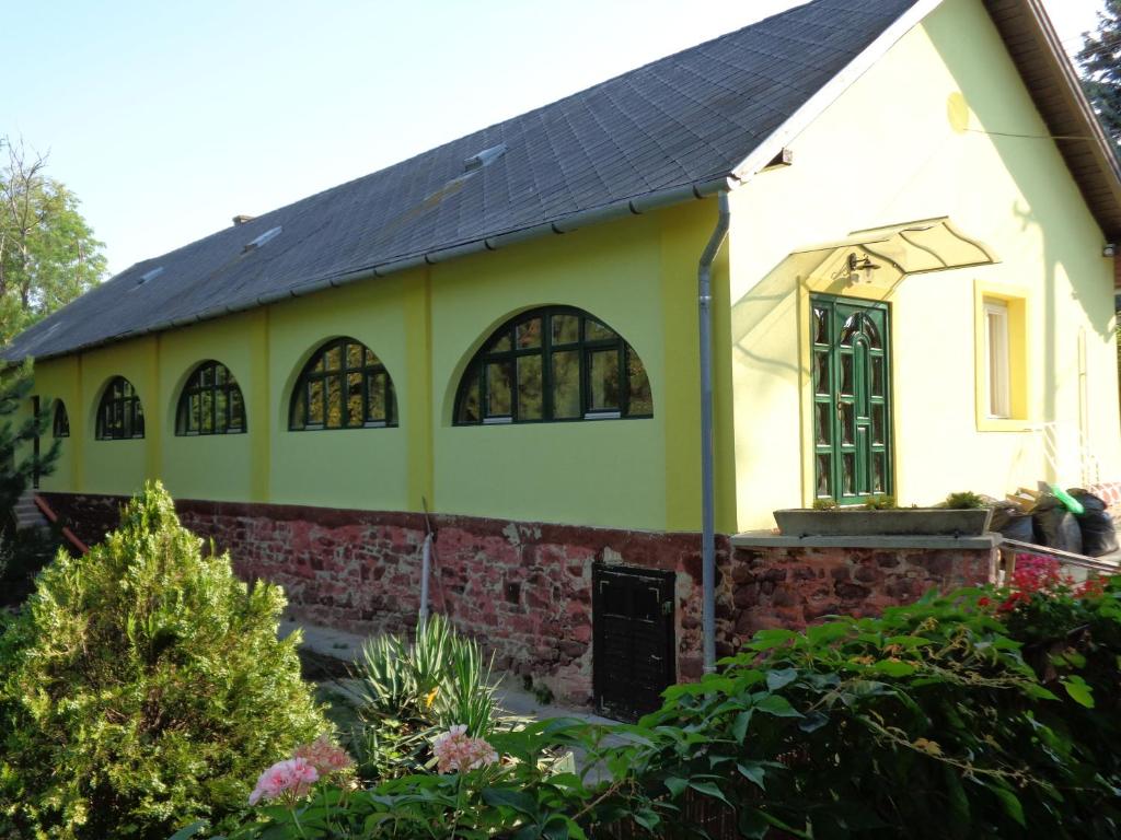 une petite maison jaune avec un toit noir dans l'établissement Árnyas Park Apartmanház, à Balatonalmádi