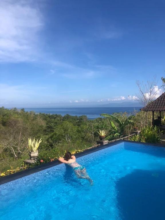 een persoon in een zwembad met de oceaan op de achtergrond bij Kaylas Hill Resort in Nusa Penida