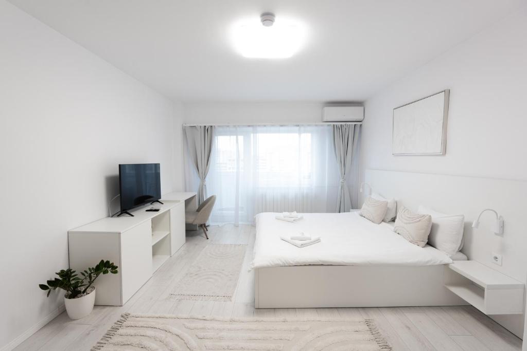 a white bedroom with a bed and a tv at Lun Apartment in Cluj-Napoca