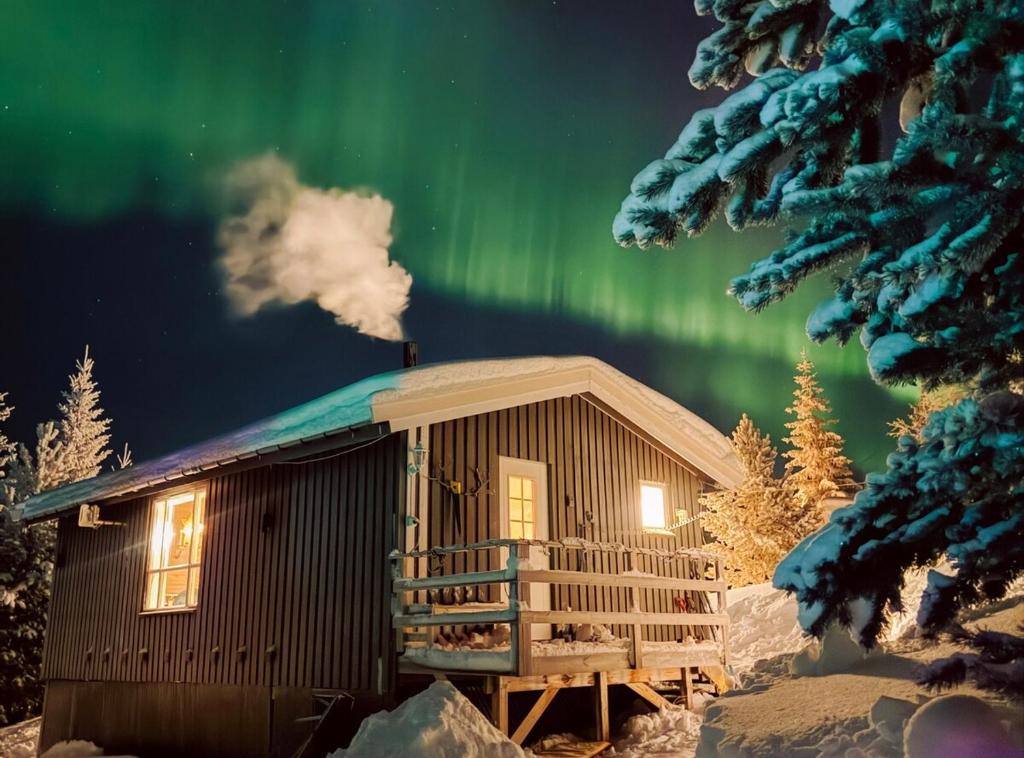 una cabaña en la nieve con la aurora en el cielo en Koselig eldre hytte, en Hammerfest