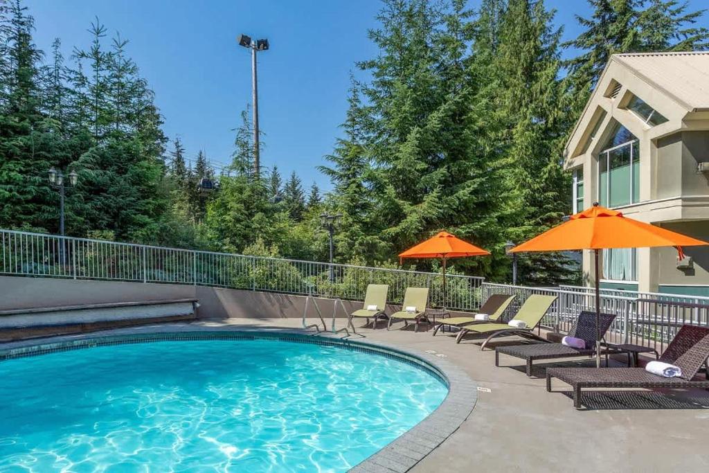 a swimming pool with chairs and umbrellas next to a house at Woodrun Lodge 217 | Ski-In Ski-Out Condo - Walk to Upper Village w/ Hot Tub, Pool + Free Parking in Whistler