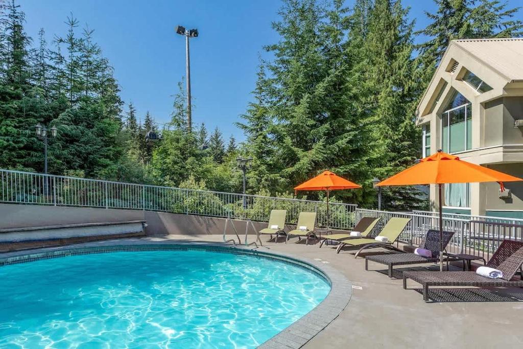 a swimming pool with chairs and umbrellas next to a house at Woodrun Lodge 517 | Large Ski-In Ski-Out Condo by Upper Village w/ Mountain Views & Shared Hot Tub in Whistler