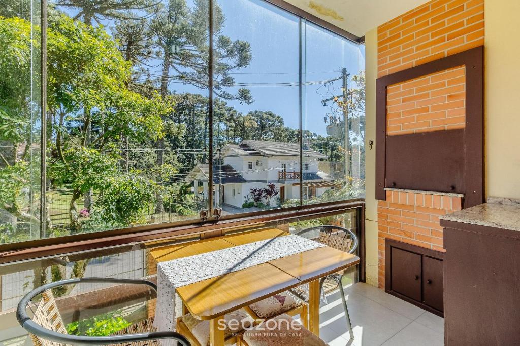 ein Balkon mit Tisch und Stühlen und einem großen Fenster in der Unterkunft Apto 300m do lago negro em Gramado/RS RLN0104 in Gramado