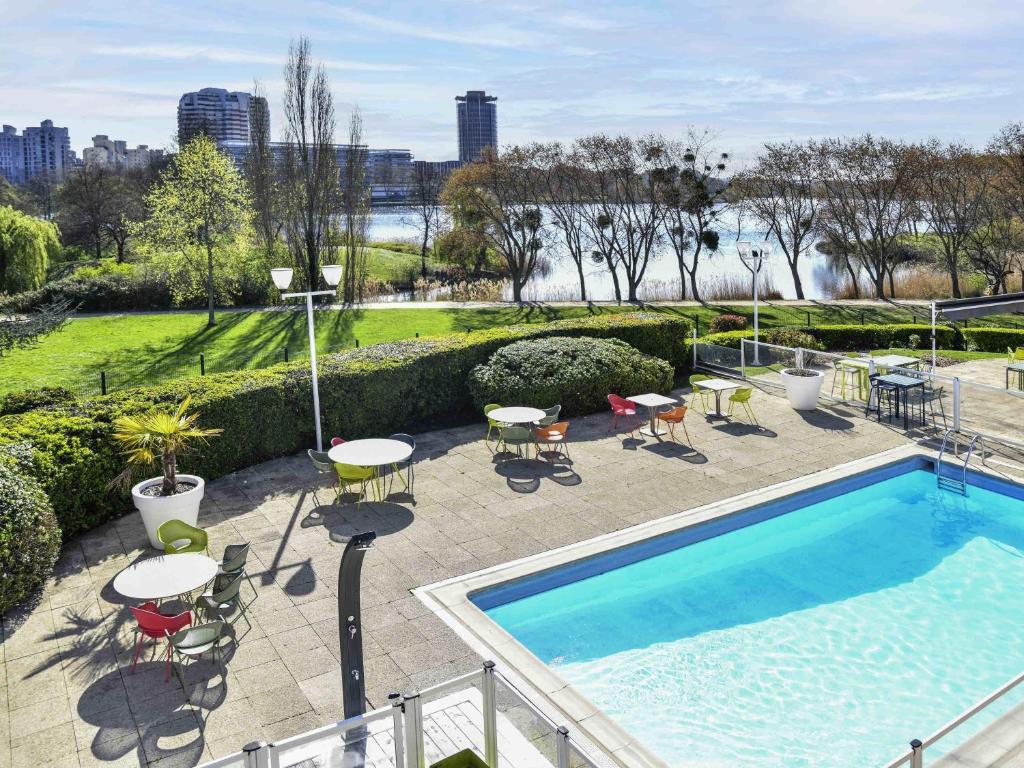 una piscina con mesas y sillas en un patio en Novotel Paris Créteil Le Lac, en Créteil
