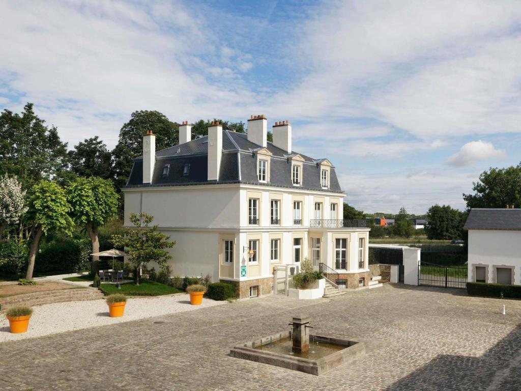 a large white house with a roof at Novotel Saclay in Saclay