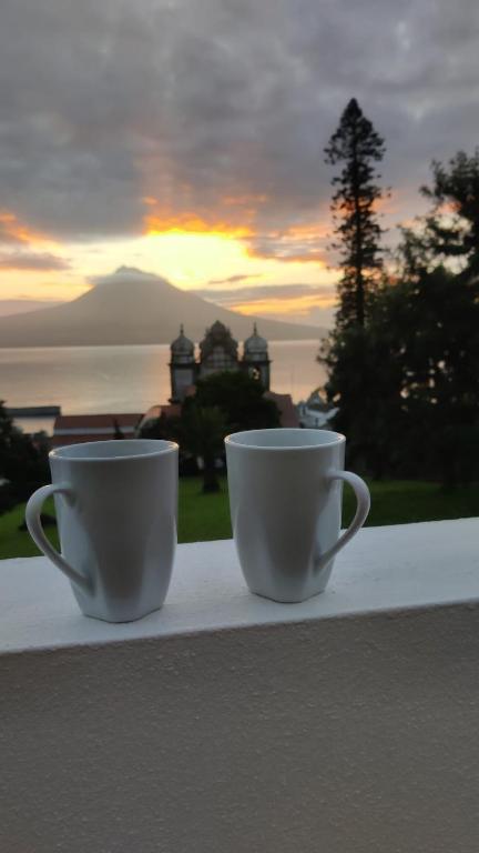 two coffee cups sitting on a ledge with a view of the ocean at Entre Ilhas in Horta