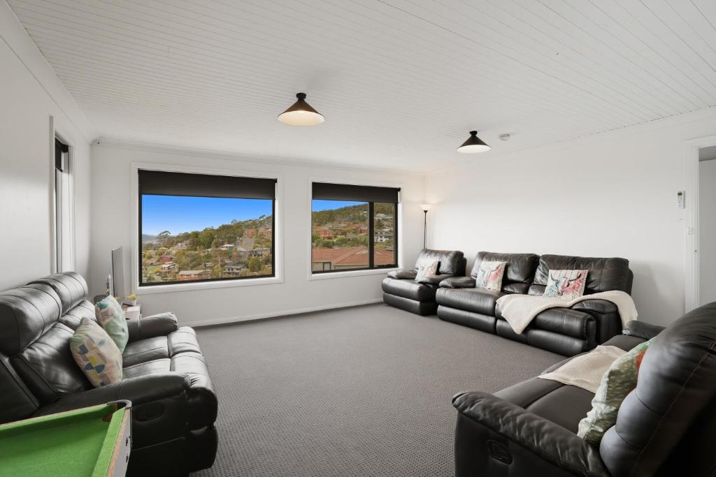 a living room with two leather couches and two windows at Large House, Centrally Located With Amazing Views in Lenah Valley