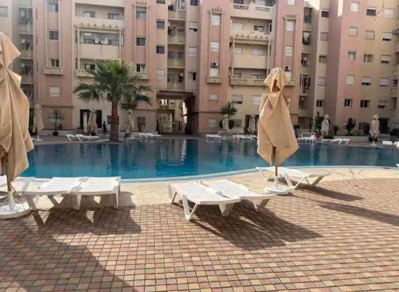 Una piscina con sillas y sombrillas frente a un edificio. en Bougainvilier, en Mohammedia