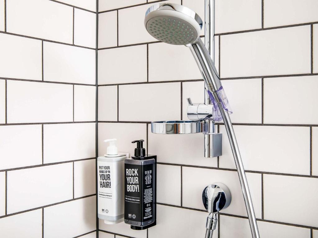 a white tiled bathroom with a blow dryer and a shower head at ibis Epinal Centre in Épinal