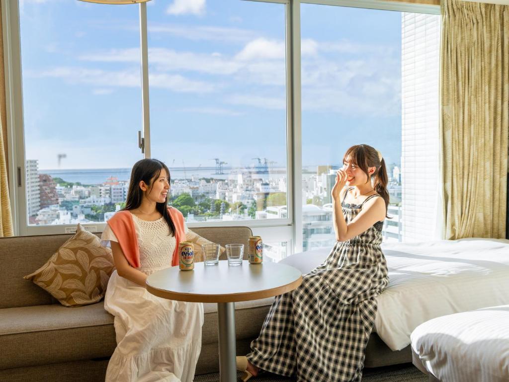 two women sitting in a hotel room with a table and a window at Nishitetsu Resort Inn Naha in Naha