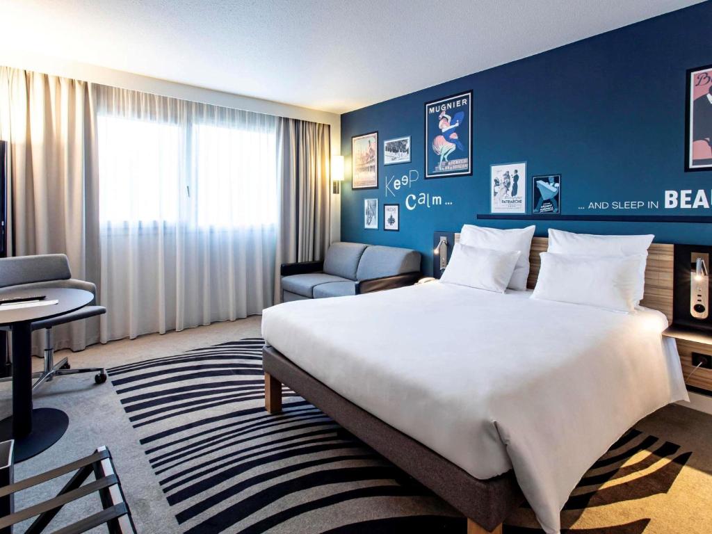 a hotel room with a large bed and a chair at Novotel Beaune in Beaune