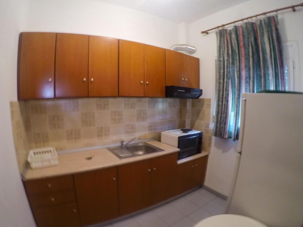 een keuken met houten kasten, een wastafel en een magnetron bij Ioannis Avrades Apartments in AgiaKampos