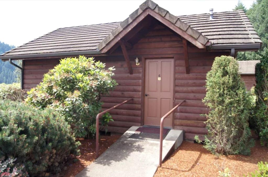 a small wooden cabin with a door and some bushes at Cozy Cabin Rental for a Camping Retreat on the Umpqua River in Oregon in Elkton