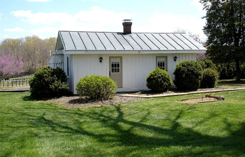a small white house in a yard with bushes at Pre-Civil War Servants' Cottage on Huge Horse and Cattle Farm near Charlottesville, Virginia in Gordonsville