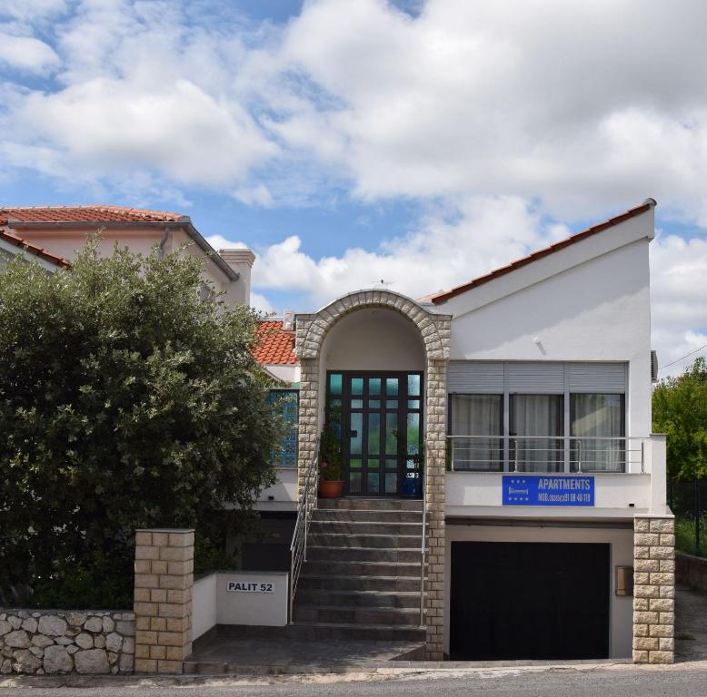 a white house with a blue sign in front of it at Apartments Crobeg in Rab
