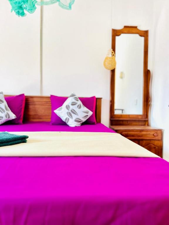 a large bed with pink and white sheets and a mirror at Nethu Freedom Cottage in Weligama