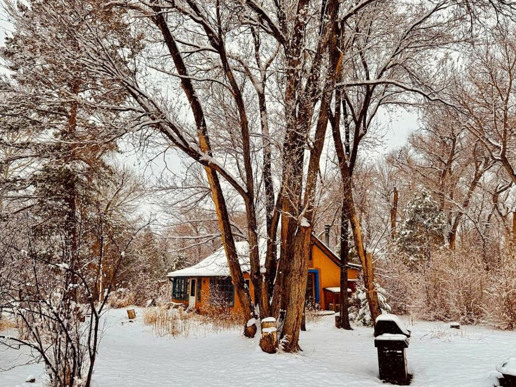 une petite maison dans la neige à côté d'un arbre dans l'établissement Artistic Garden Casita on Organic Farm in New Mexico, à San Cristobal