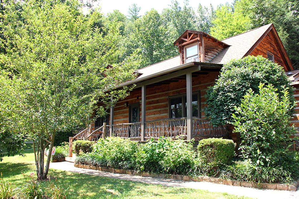 une cabane en rondins avec une véranda et des arbres dans l'établissement Rustic Log Cabin Rental with a Hot Tub near Asheville, North Carolina, à Crabtree