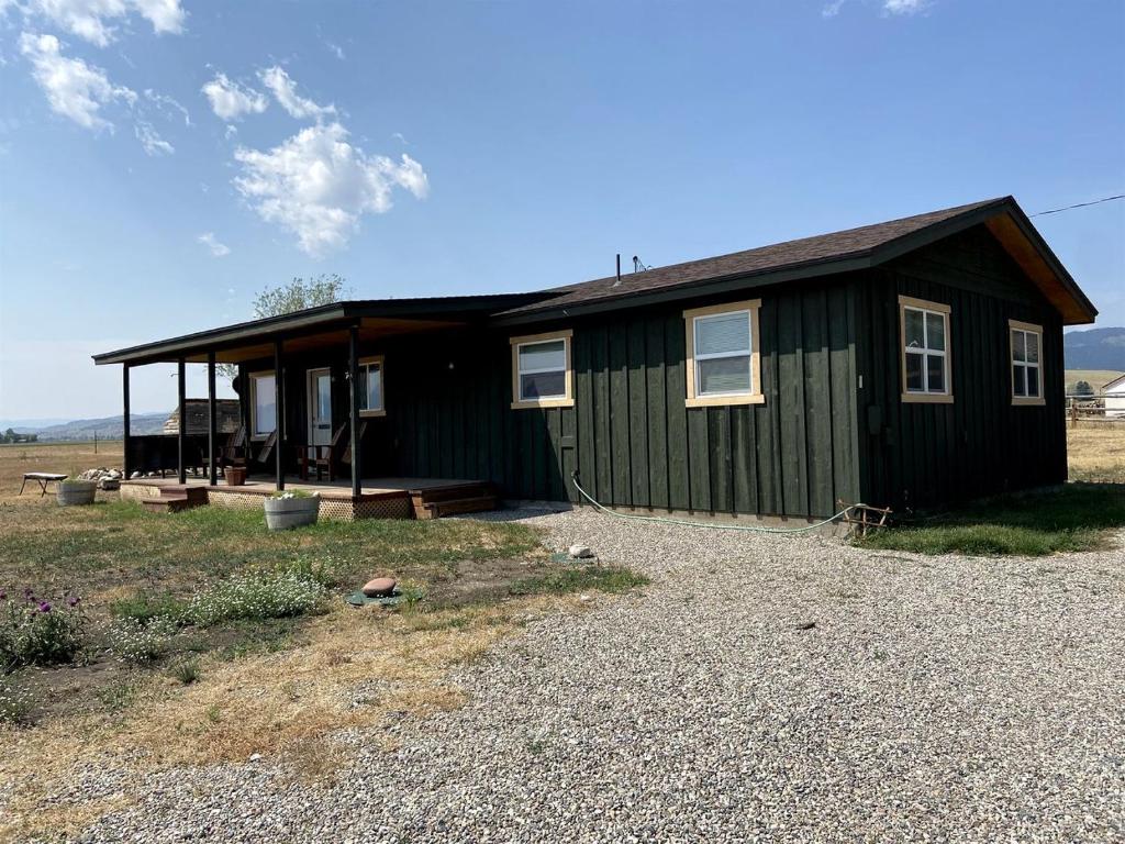 a small green house with a porch on a field at Secluded Modern Vacation Home with Madison Range Views near Ennis Lake, McAllister Montana in Ennis