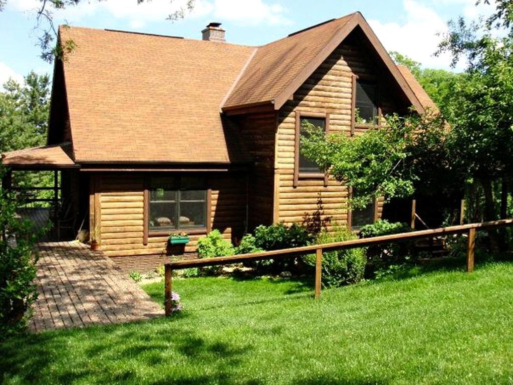 a wooden house with a green lawn in front of it at Luxury Log Cabin with 18 Acres of Countryside and Swimming Pond near Athens, Ohio in Athens