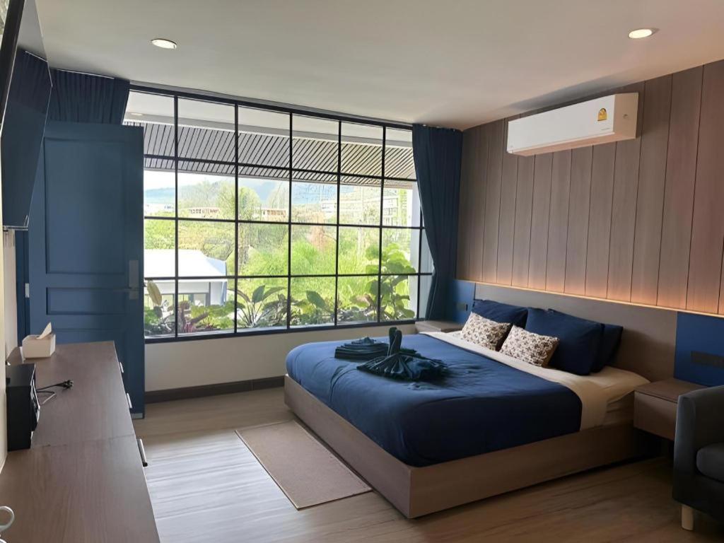a bedroom with a blue bed and a large window at Calm Kamala Phuket in Kamala Beach