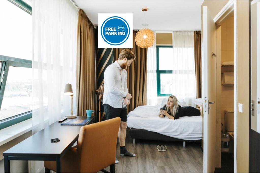 a man standing in a hotel room with a woman laying on a bed at The Hague Teleport Hotel in The Hague