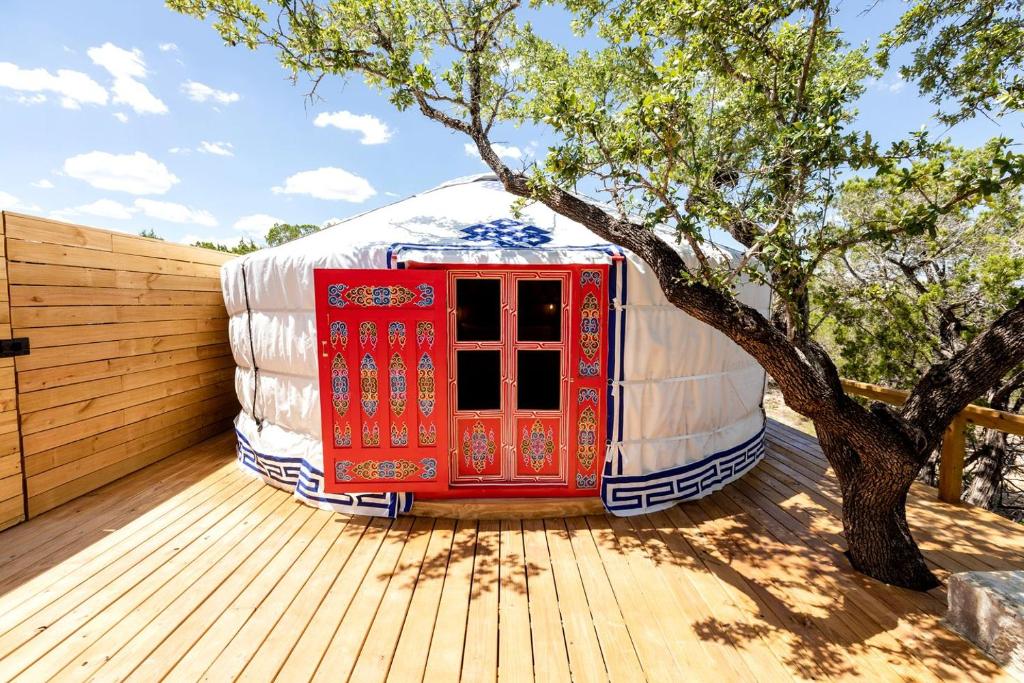 a yurt with a red door next to a tree at Cozy Yurt with Hot Tub Surrounded by Nature in Dripping Springs, Texas in Hammetts Crossing