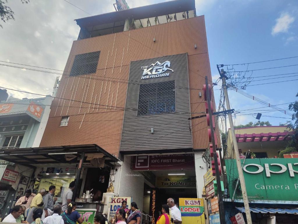 una multitud de personas de pie fuera de un edificio en Hotel O The KG Meridian, en Ambāsamudram