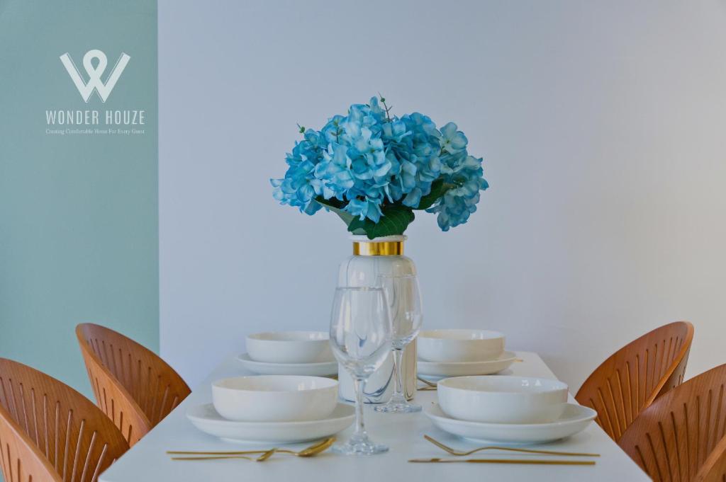 a table with plates and a vase with blue flowers at Modern Stay at Seri Kembangan - 20 mins to Pavilion Bukit Jalil in Seri Kembangan