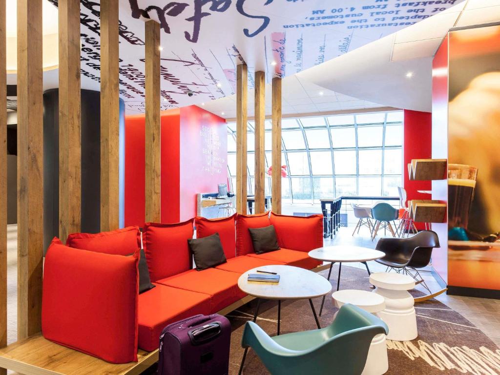 A colourful hotel lobby lounge with red seating, small tables and mixed chairs.