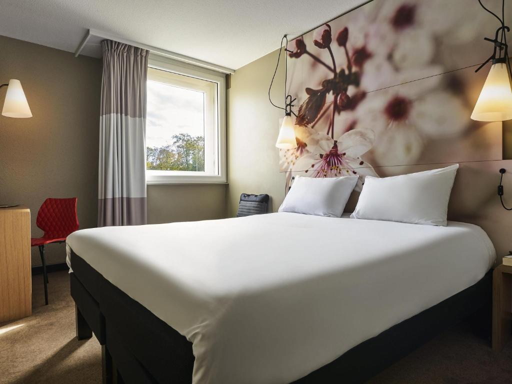 a hotel room with a large bed and a window at ibis Paris Marne la Vallee Emerainville in Émerainville