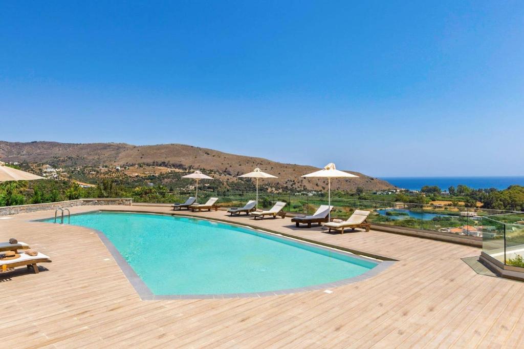 a swimming pool with chairs and umbrellas and the ocean at Villa Lefkothea by Villa Plus in Georgioupoli