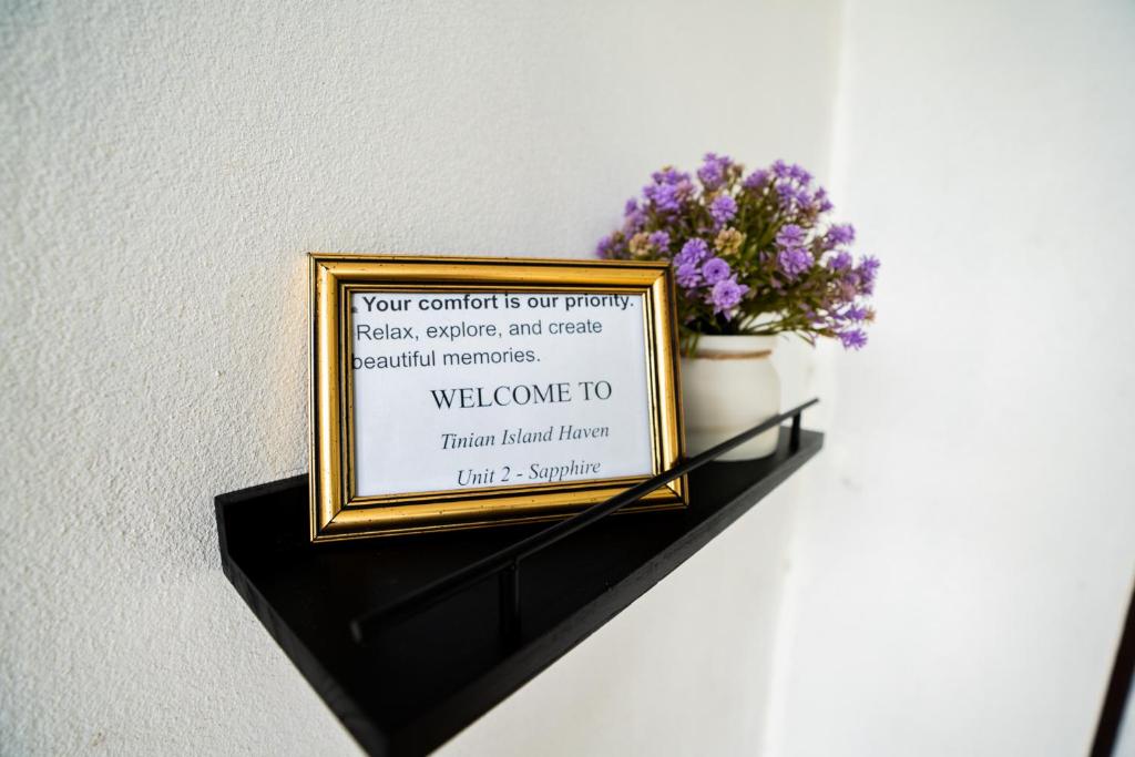un panneau encadré sur une étagère avec des fleurs dessus dans l'établissement Tinian Island Haven, Sapphire Unit Apartment, 