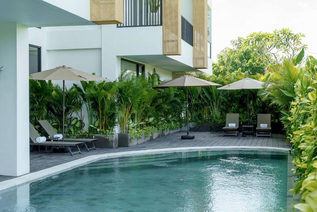 une piscine avec chaises et parasols à côté d'un bâtiment dans l'établissement Sunny Aparts 1, à Canggu