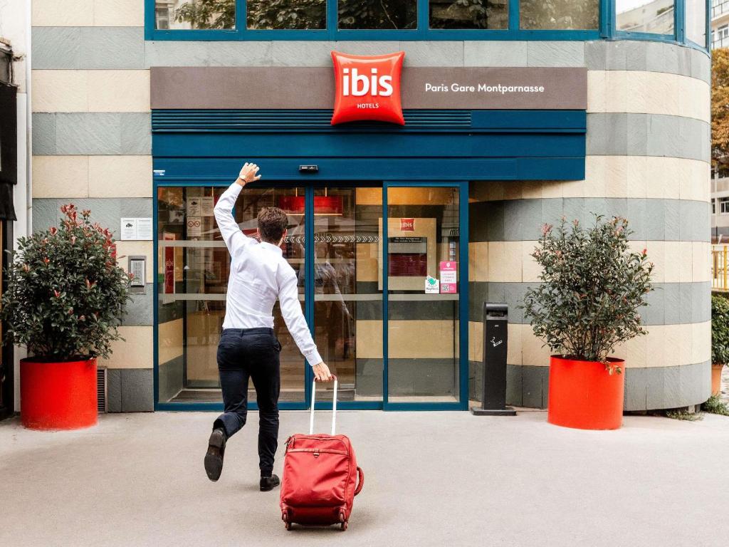 パリにあるIbis Paris Gare Montparnasse 15èmeの赤いスーツケースを引き寄せた男