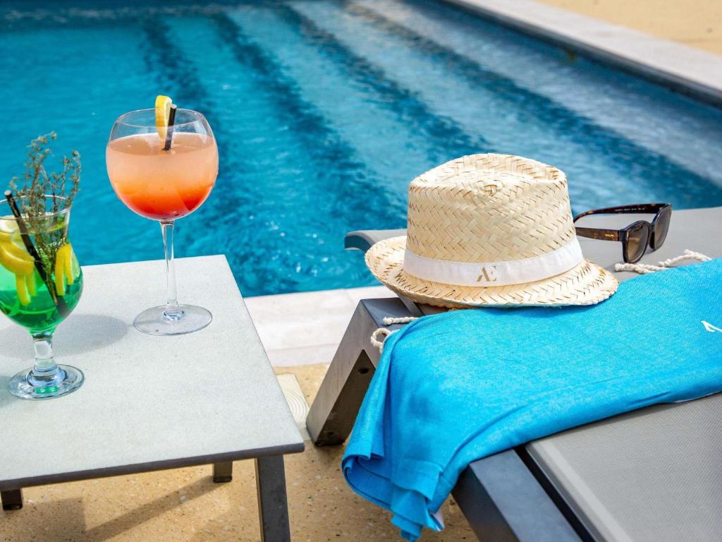 a hat and a drink on a table next to a pool at Mercure Cavaillon in Cavaillon