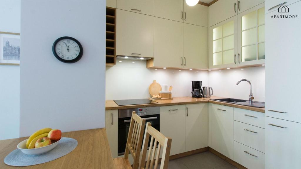 Modern L-shaped kitchen with wooden countertops, under-cabinet lighting, wall clock and fruit bowl.